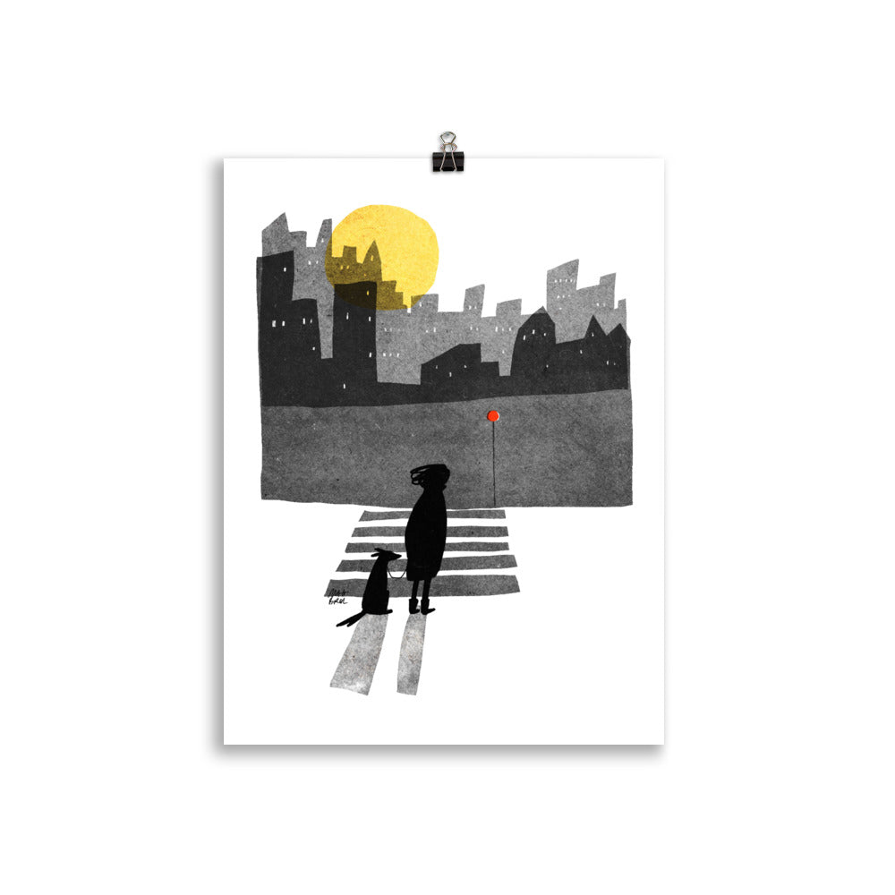 Across art print by Magda Brol: a woman and her dog crossing a zebra crossing at night under a yellow moon, with a dark city skyline, unframed print hanging from a clip
