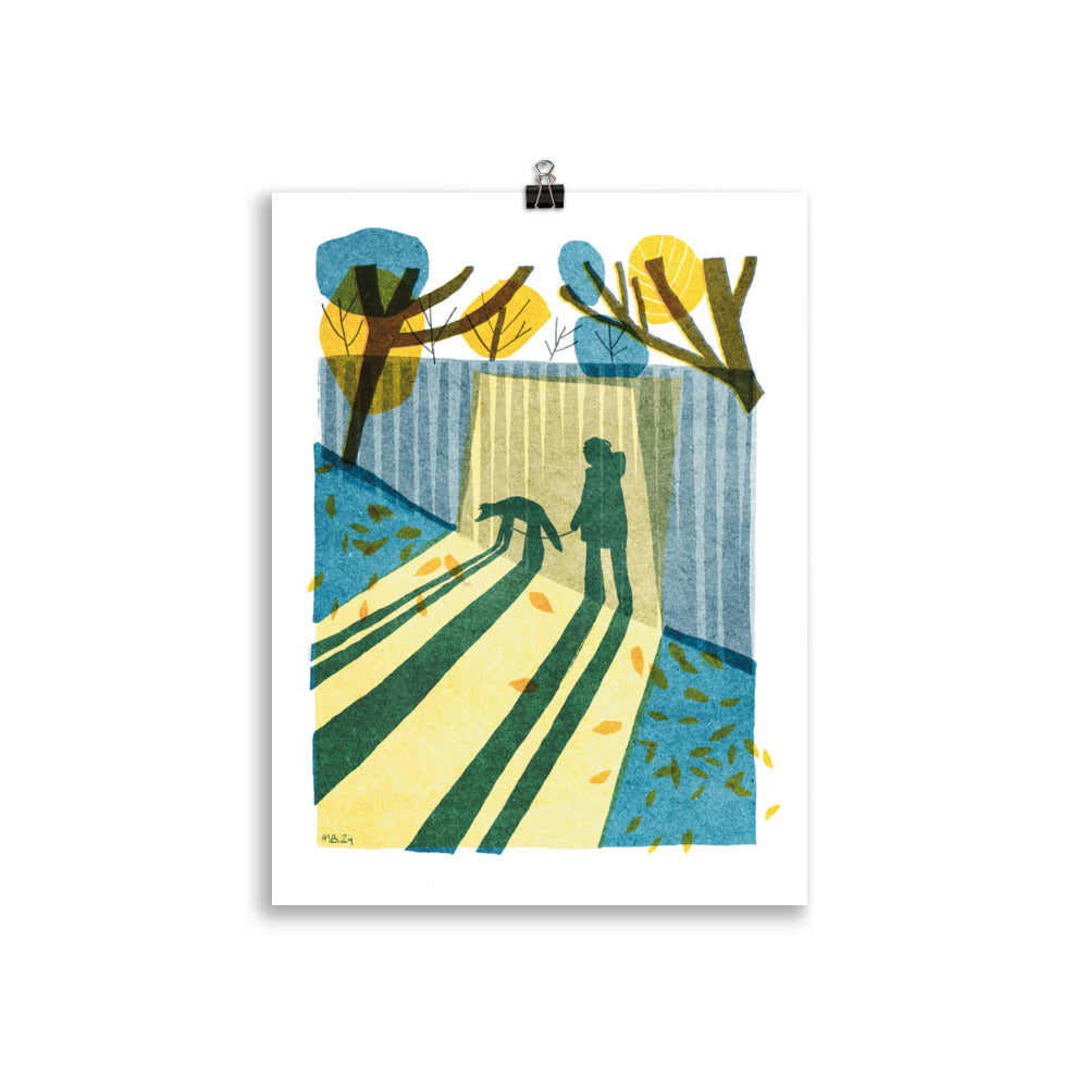 Morning shadow art print by Magda Brol: a woman and her dog casting long shadows beside a fence on an autumn morning, in yellow, teal and blue, unframed print hanging from a clip